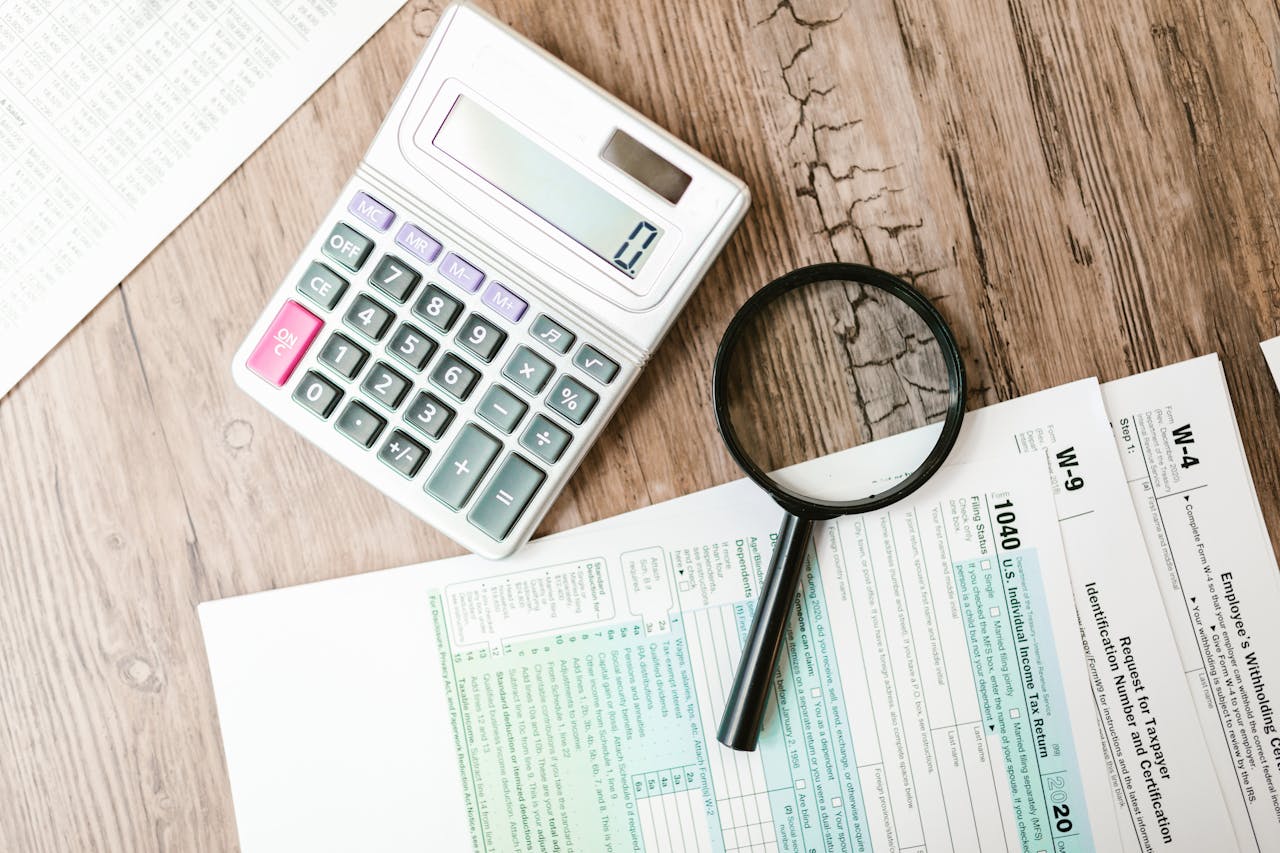 home-services-004 Tax forms laid out with a calculator and magnifying glass on a wooden surface, perfect for finance themes.