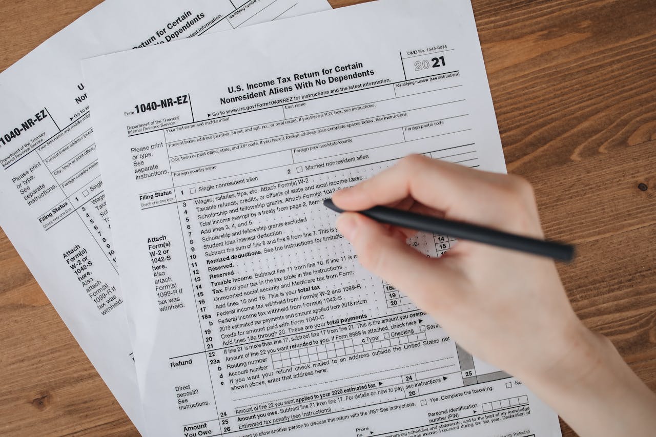 cta-bg Person filling out U.S. tax form 1040-NR-EZ with a pen on a wooden table.