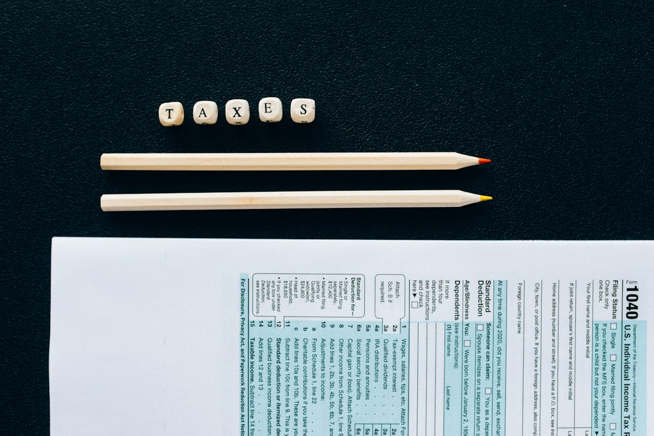 about-01 Flat lay of 1040 tax form with pencils and TAXES blocks on black background.